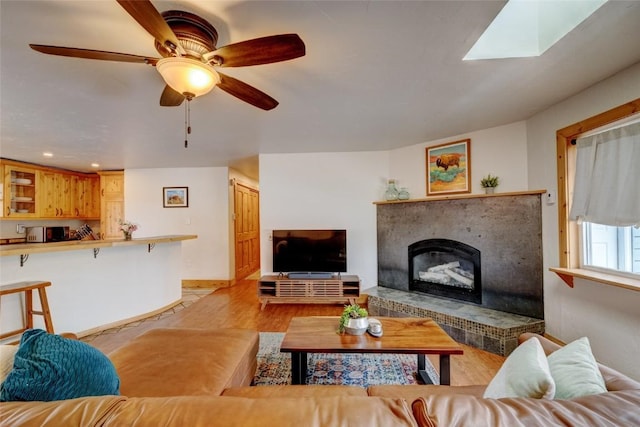 living area featuring ceiling fan, a fireplace with raised hearth, light wood-style flooring, recessed lighting, and baseboards