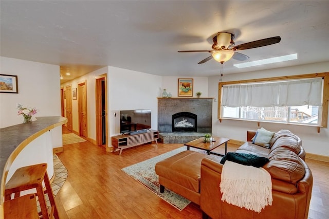 living room featuring baseboards, a fireplace with raised hearth, a ceiling fan, and light wood-style flooring