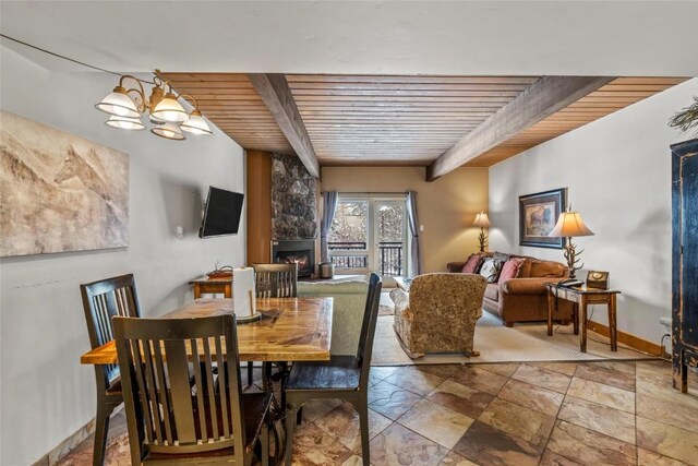 dining room with beam ceiling, a chandelier, stone finish flooring, wooden ceiling, and a stone fireplace