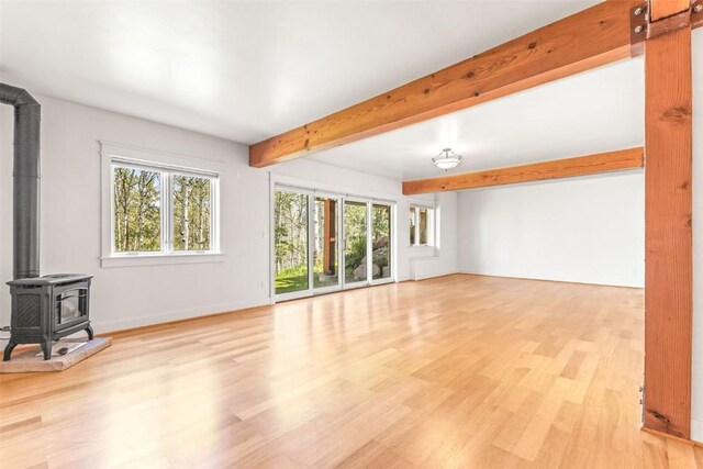 31820 Bradley Rnch, Steamboat Springs, CO 80487 - unfurnished living room with beamed ceiling, light wood-style flooring, a wood stove, healthy amount of natural light, and baseboards