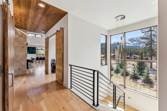 427 Whispering Pines Cir, Blue River, CO 80424 - corridor with a barn door, light wood-style floors, wood ceiling, a mountain view, and an upstairs landing