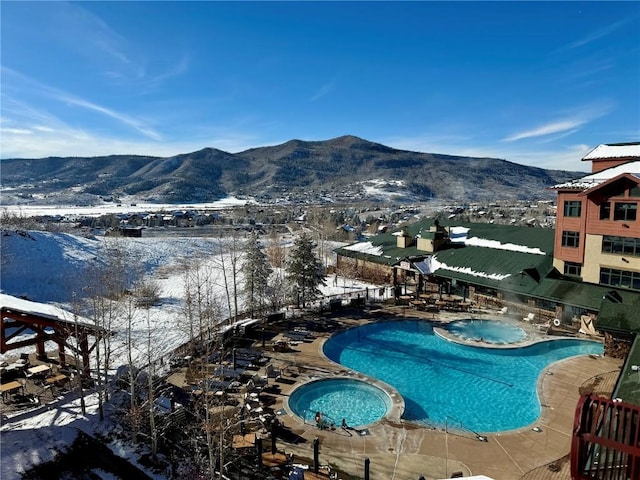 snow covered pool featuring a pool with connected hot tub and a mountain view