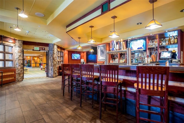 bar featuring a bar, a tray ceiling, hanging light fixtures, and decorative columns