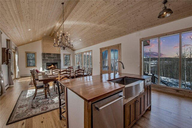 kitchen featuring lofted ceiling with beams, stainless steel dishwasher, a sink, a fireplace, and wooden counters