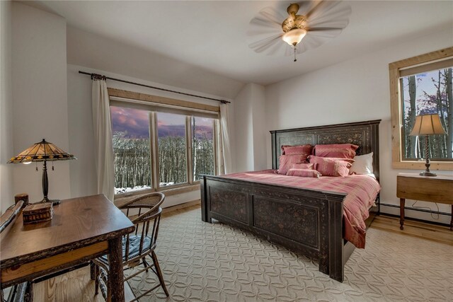 bedroom featuring a baseboard heating unit, a ceiling fan, multiple windows, and light wood-style flooring