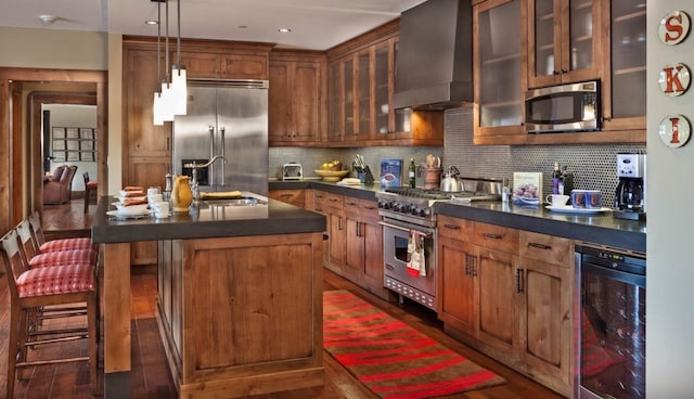 kitchen featuring dark countertops, high quality appliances, a sink, wall chimney exhaust hood, and wine cooler