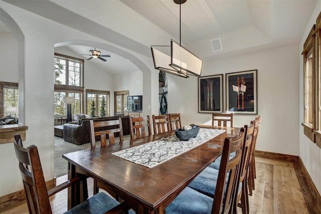 dining room with baseboards, visible vents, arched walkways, vaulted ceiling, and light wood-style floors