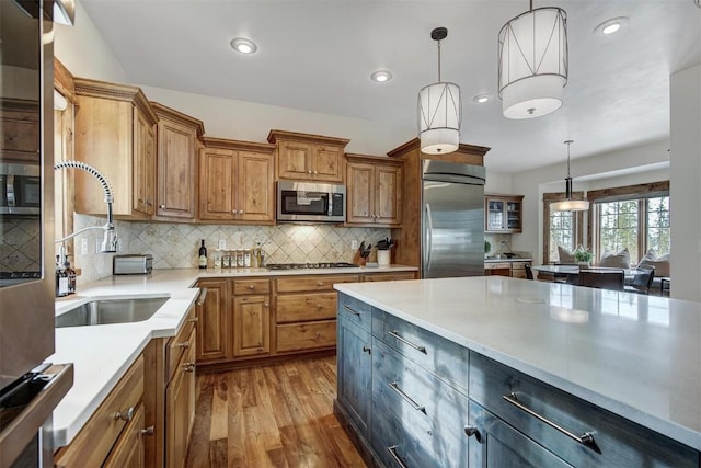 kitchen featuring stainless steel appliances, wood finished floors, light countertops, brown cabinetry, and pendant lighting