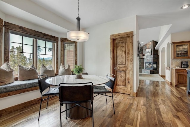 dining area featuring arched walkways, light wood finished floors, a fireplace, and baseboards