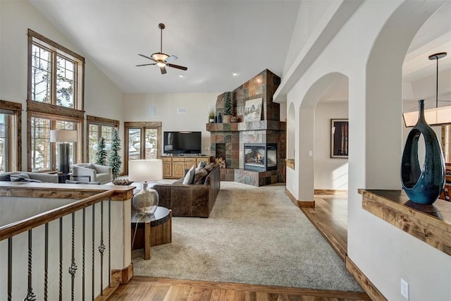 living area with high vaulted ceiling, a tiled fireplace, wood finished floors, and a ceiling fan