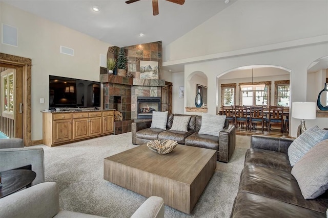 living area featuring high vaulted ceiling, a tile fireplace, light carpet, visible vents, and a ceiling fan