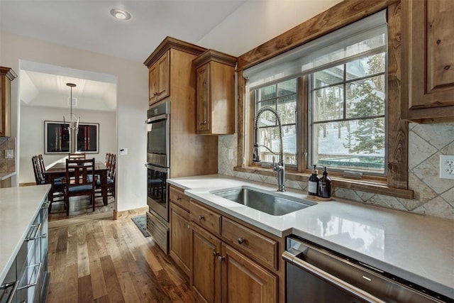 kitchen featuring brown cabinets, light countertops, double oven, a sink, and dishwasher