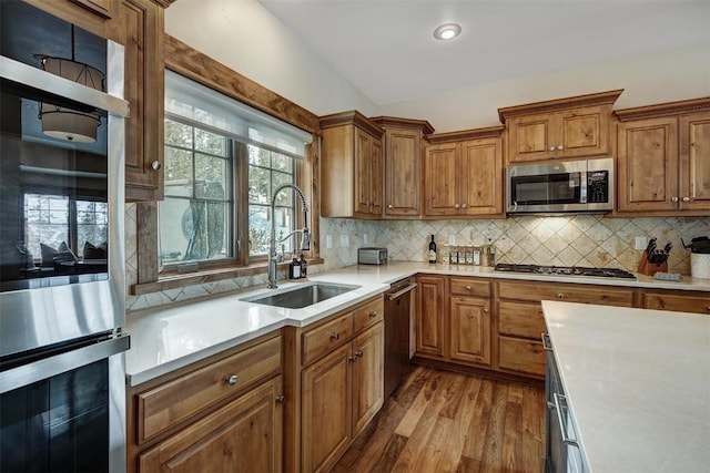 kitchen with brown cabinets, a sink, stainless steel appliances, light countertops, and backsplash