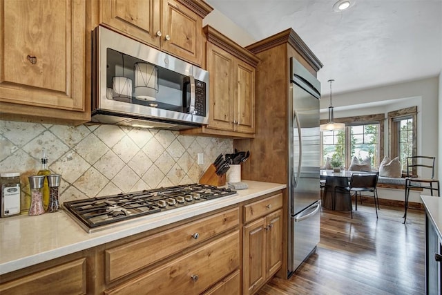 kitchen with light countertops, appliances with stainless steel finishes, brown cabinetry, and tasteful backsplash