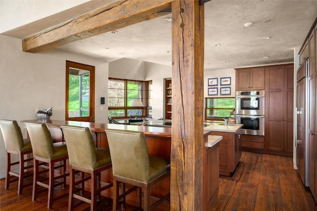 33225 Painted Pony Ln, Steamboat Springs, CO 80487 - kitchen with dark wood-style floors, double oven, beam ceiling, a kitchen breakfast bar, and a peninsula