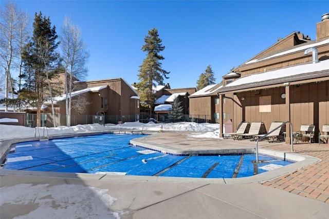 snow covered pool featuring a community pool, fence, and a patio area