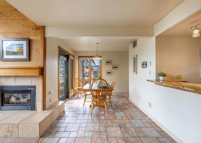 dining area with visible vents, a tiled fireplace, beam ceiling, baseboards, and stone tile flooring