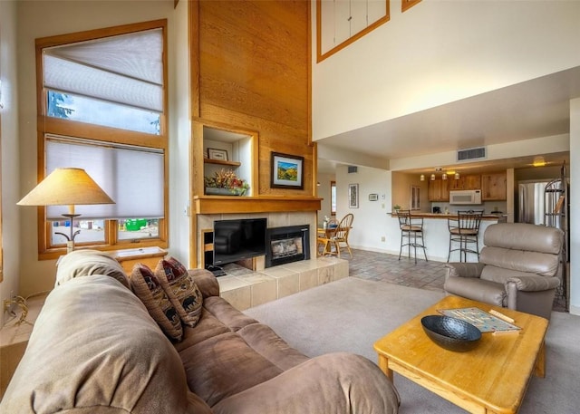living area featuring visible vents, baseboards, a high ceiling, and a tile fireplace