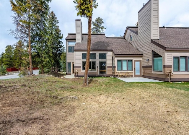 rear view of house featuring a patio, roof with shingles, a yard, and a chimney