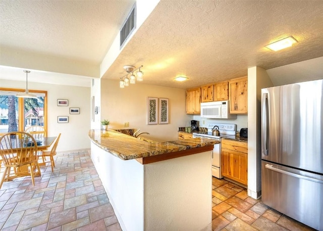 kitchen with white appliances, a textured ceiling, stone tile floors, a peninsula, and visible vents