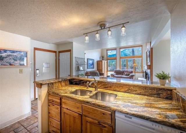 kitchen with brown cabinets, white dishwasher, light stone counters, and a sink