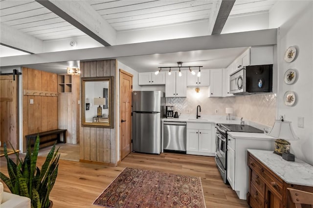 kitchen featuring white cabinets, beam ceiling, a sink, light wood-type flooring, and appliances with stainless steel finishes