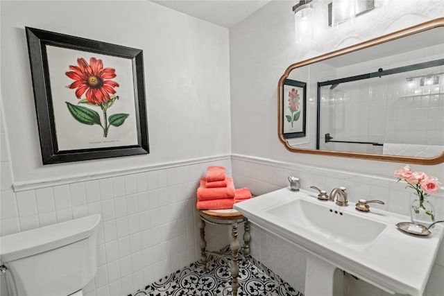 bathroom featuring wainscoting, toilet, a shower with door, and tile walls