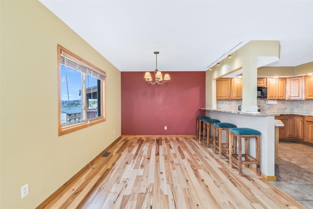 kitchen featuring an inviting chandelier, black microwave, a kitchen breakfast bar, light wood finished floors, and backsplash
