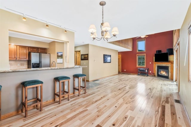 kitchen featuring brown cabinets, a breakfast bar, a chandelier, light wood-type flooring, and refrigerator with ice dispenser