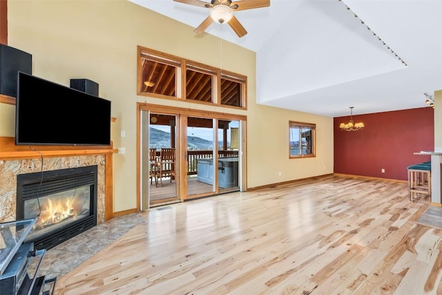 unfurnished living room with a tiled fireplace, baseboards, ceiling fan with notable chandelier, and wood finished floors