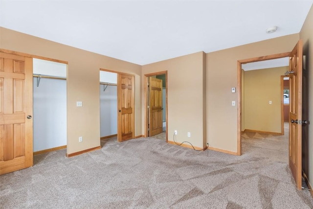 unfurnished bedroom featuring carpet floors, baseboards, and two closets
