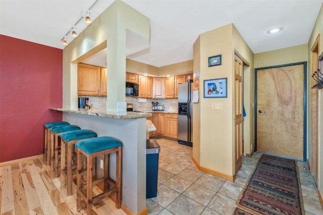 kitchen featuring black microwave, stainless steel fridge, a peninsula, baseboards, and a kitchen bar