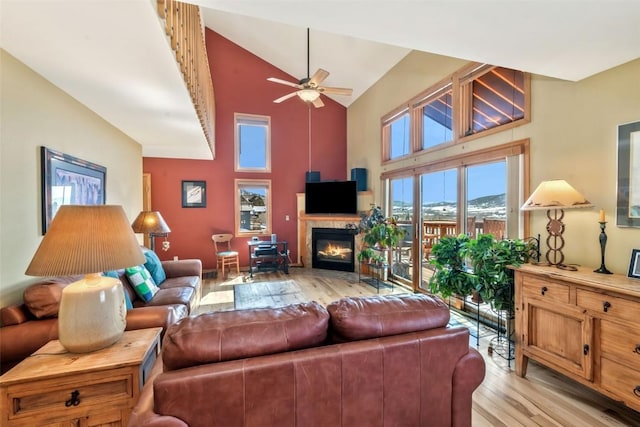 living area featuring a glass covered fireplace, high vaulted ceiling, ceiling fan, and light wood-style flooring