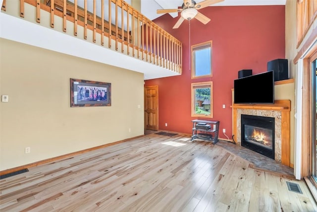 unfurnished living room with a glass covered fireplace, a ceiling fan, wood finished floors, a towering ceiling, and visible vents