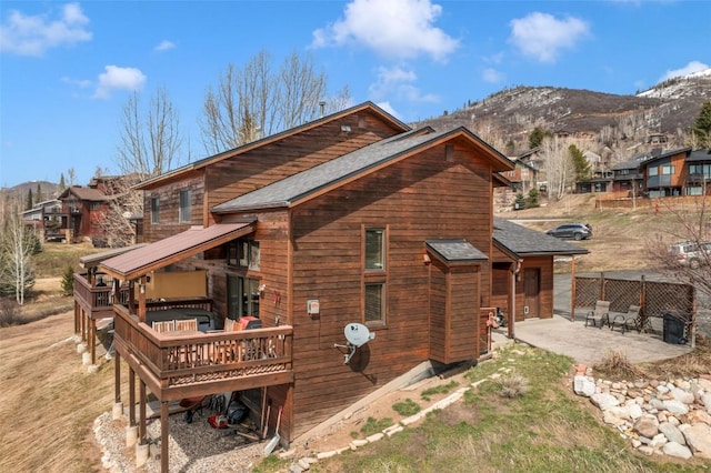 rear view of house with a patio, a deck with mountain view, and a shingled roof