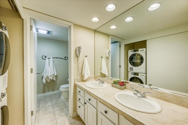 bathroom featuring double vanity, toilet, stacked washer / dryer, and a sink