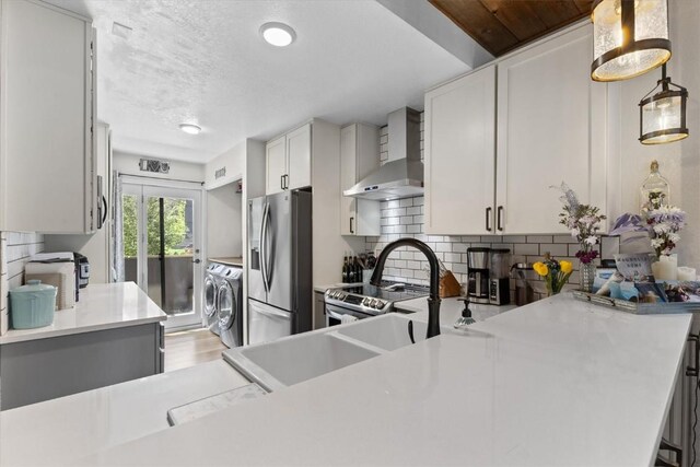 2146 Aster Pl Unit 3, Steamboat Springs, CO 80487 - kitchen featuring washer and dryer, wall chimney range hood, stainless steel appliances, light countertops, and backsplash