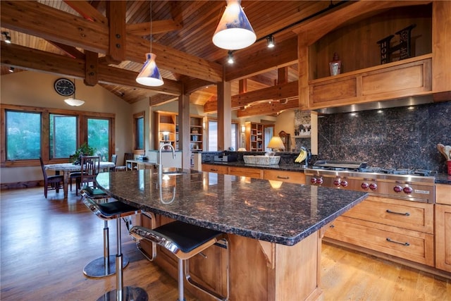 35525 Humble Rd, Steamboat Springs, CO 80487 - kitchen featuring stainless steel gas cooktop, decorative backsplash, a breakfast bar area, light wood-style floors, and dark stone counters