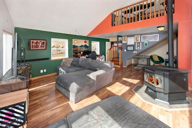 living room with wood finished floors, a wood stove, stairs, baseboards, and high vaulted ceiling