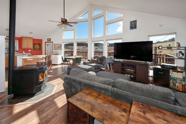 living area featuring wood finished floors, a wood stove, high vaulted ceiling, and ceiling fan