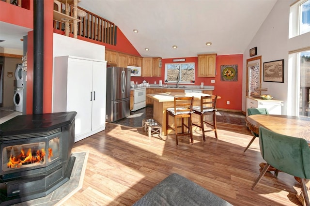 kitchen with high vaulted ceiling, stacked washing maching and dryer, white appliances, a wood stove, and light countertops