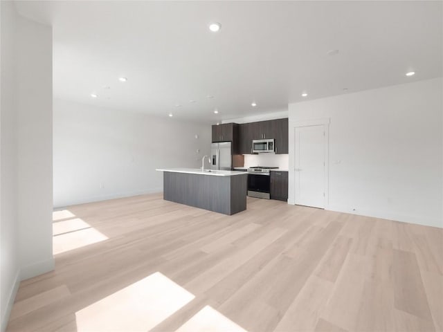 740 Blue River Pkwy Unit A22, Silverthorne, CO 80498 - kitchen featuring stainless steel appliances, open floor plan, a kitchen island with sink, light countertops, and light wood finished floors