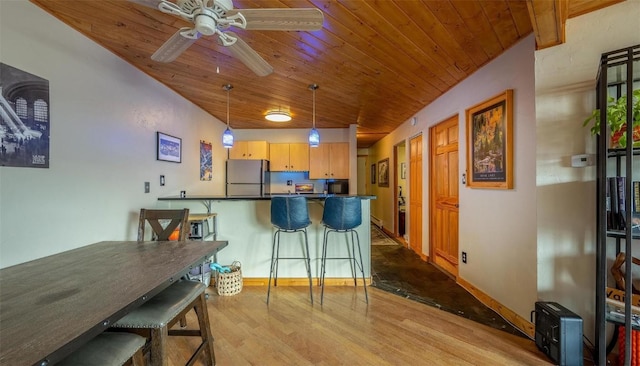 kitchen featuring a peninsula, fridge, dark countertops, wood finished floors, and a breakfast bar