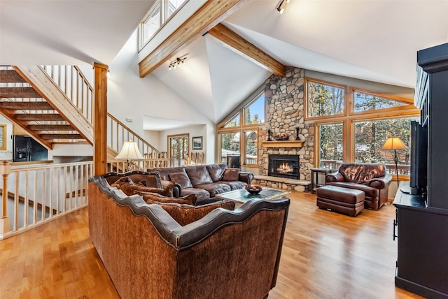 living room featuring high vaulted ceiling, light wood-style floors, a fireplace, rail lighting, and beam ceiling