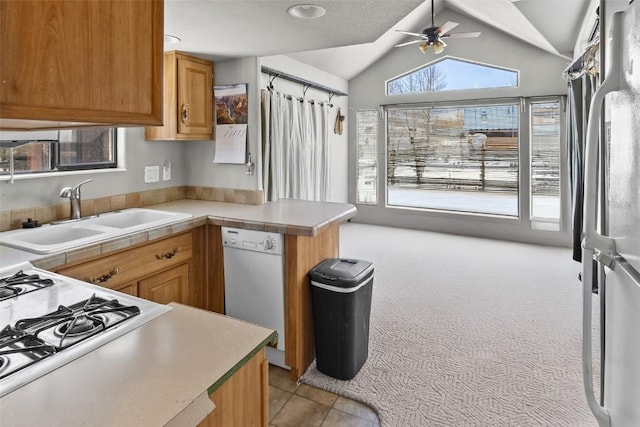 kitchen featuring a peninsula, a sink, vaulted ceiling, white dishwasher, and a ceiling fan
