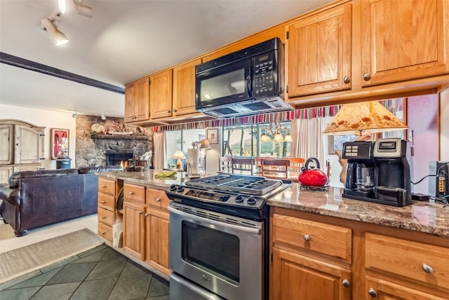kitchen featuring stainless steel range with gas stovetop, open floor plan, black microwave, dark tile patterned flooring, and a fireplace