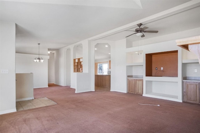 unfurnished living room featuring baseboards, carpet, ceiling fan with notable chandelier, and built in shelves
