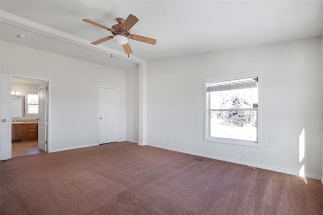 unfurnished bedroom featuring light colored carpet, baseboards, ensuite bathroom, and multiple windows