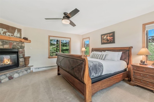 bedroom with carpet flooring, a ceiling fan, a stone fireplace, and baseboard heating
