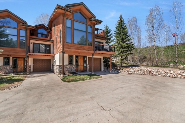 view of front of house with a garage, stone siding, driveway, and a balcony